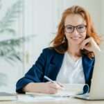 Happy successful female writes checklist in notepad, works on creative ideas for project