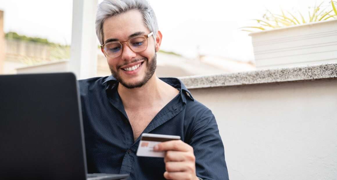 Young hipster man holding credit cart using computer laptop for online payment - E-commerce, bank