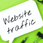 Website traffic handwritten on white speech bubble, with glasses and pen on green background.