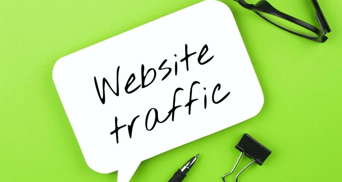 Website traffic handwritten on white speech bubble, with glasses and pen on green background.